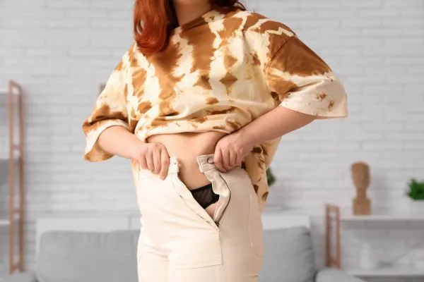 Image of woman trying to do her trousers up after pregnancy weight gain Chesham