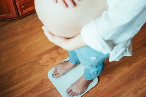 Image of woman weighing herself and experiencing weight gain through pregnancy Chesham